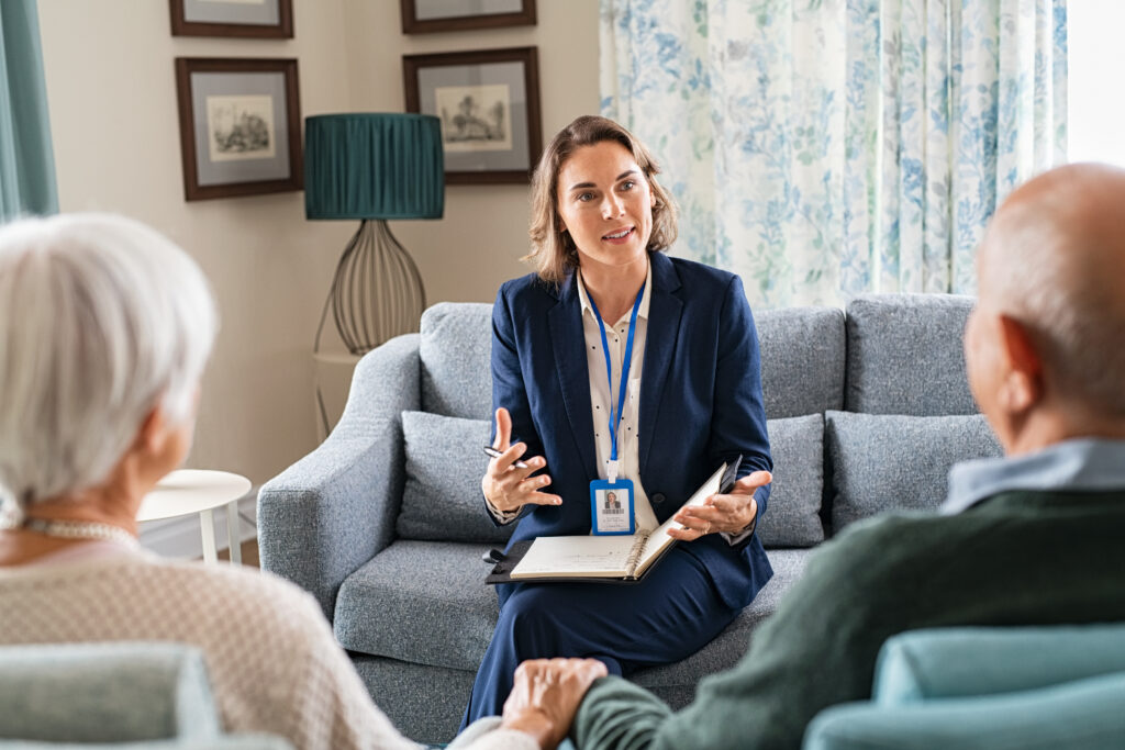 Woman insurance agent in home speaking to two seniors who appear to be married about their insurance options