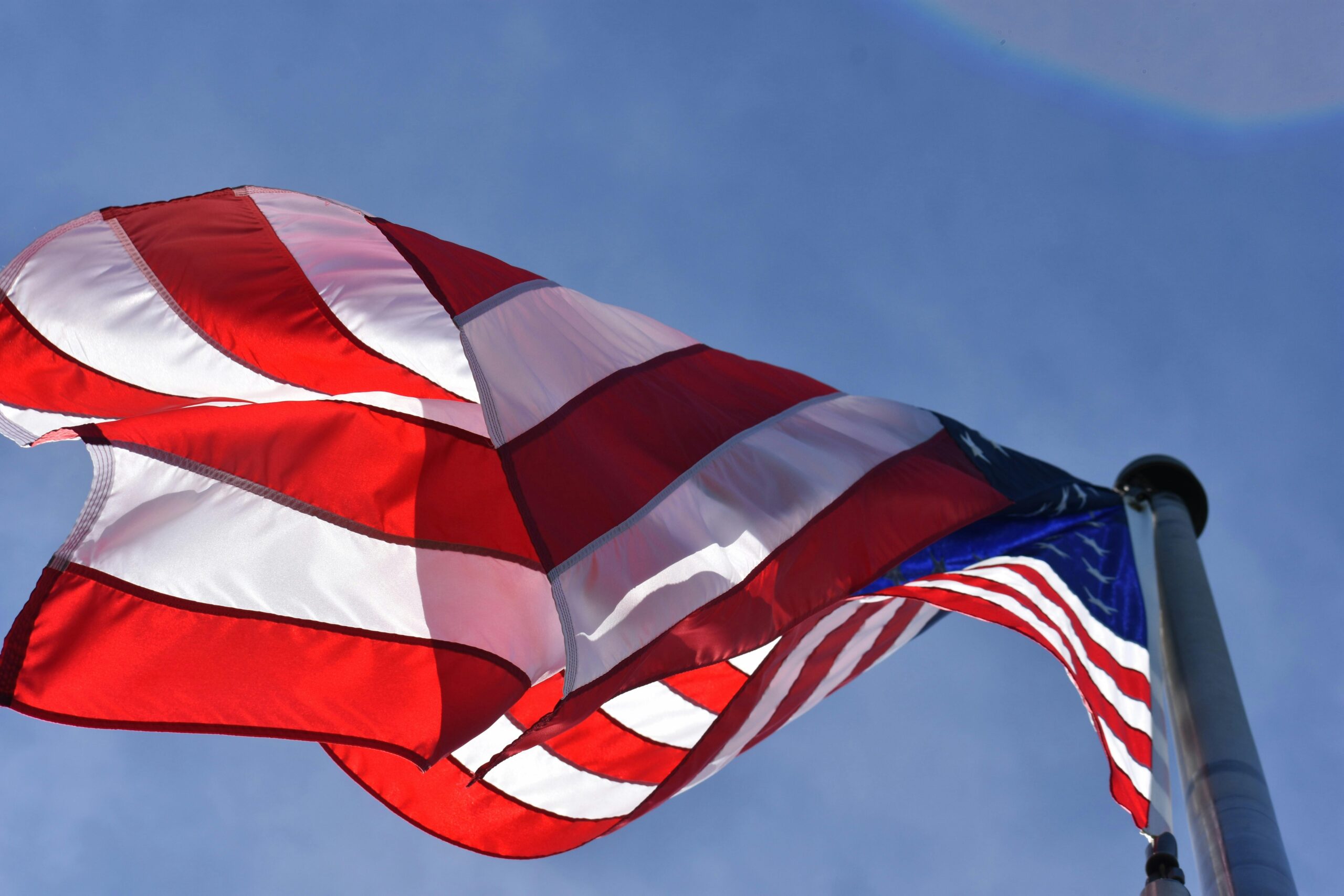 From-below shot of a large American flag on a flagpole, blowing in the wind.