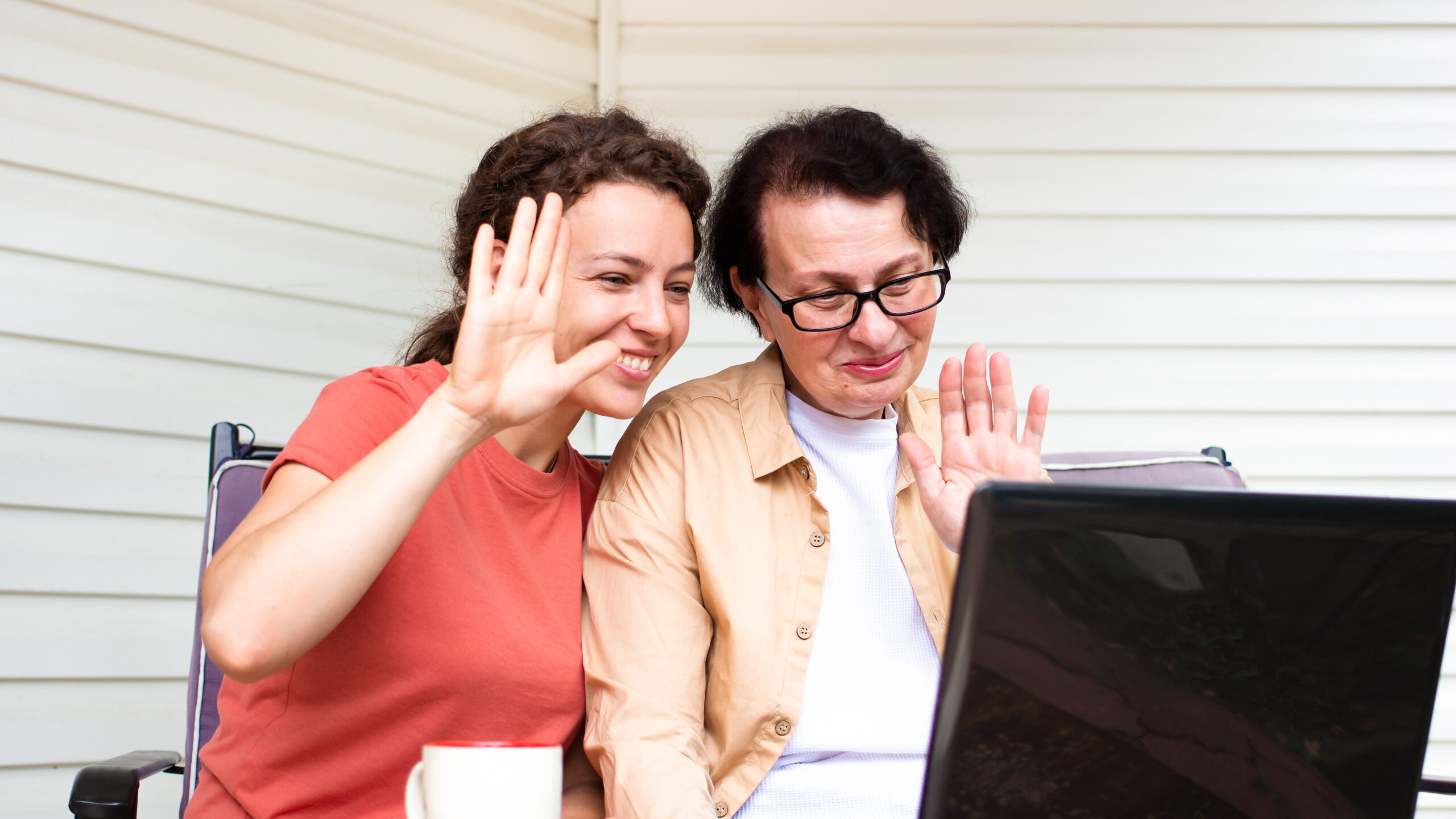 Happy mature mother with grown up daughter making video call with laptop, gesturing hi to her insurance agent