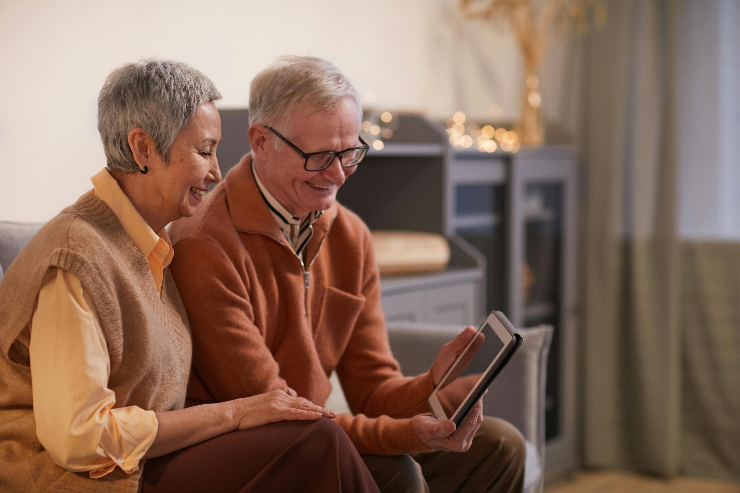 An older couple smiles while staring at a tablet.