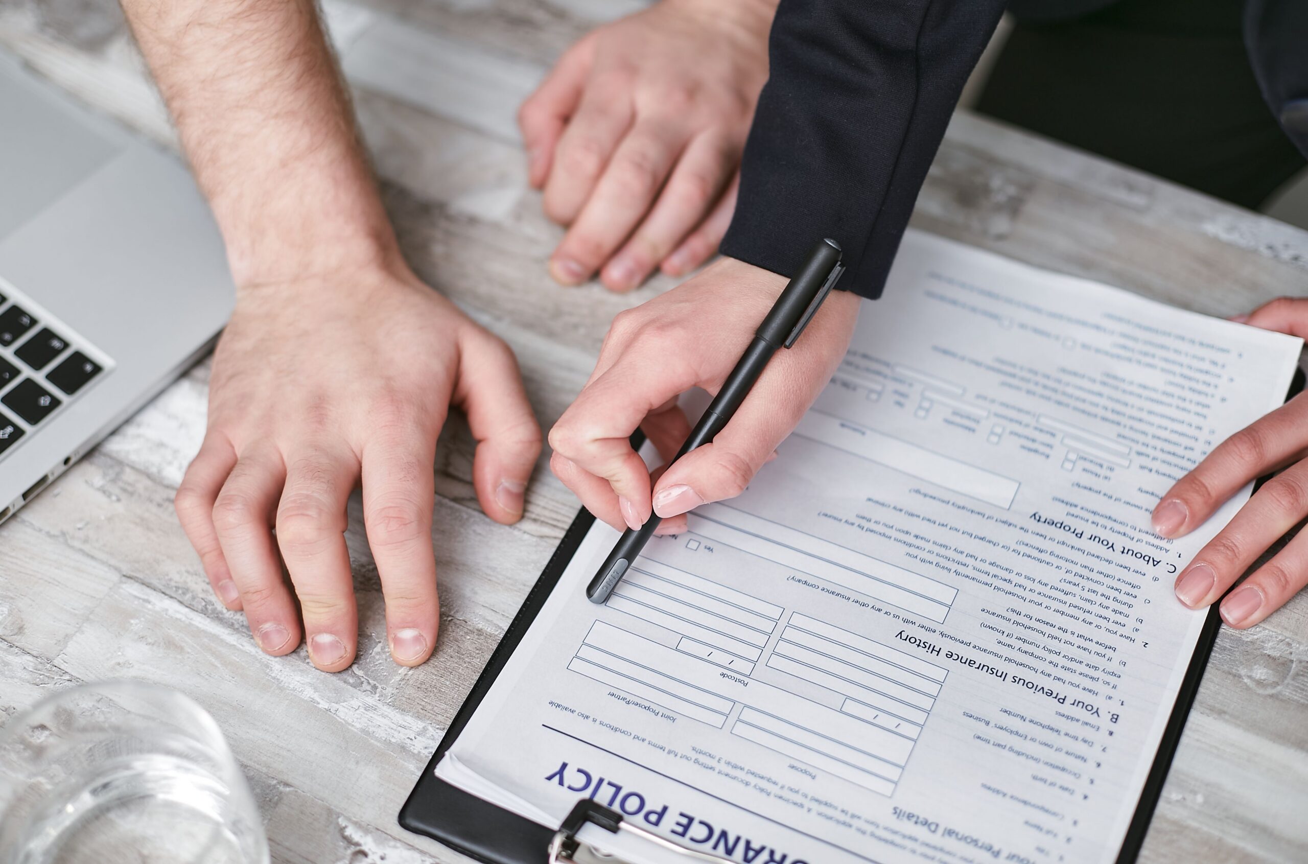 An overhead view of two people reviewing and signing an insurance policy document on a clipboard.