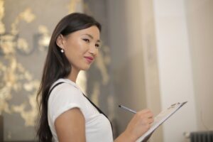 A confident young insurance agent smiles over her shoulder while writing on a clipboard.